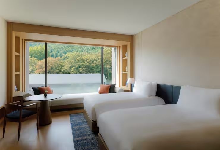Modernes Hotelzimmer mit zwei Einzelbetten und großem Fenster mit Waldblick.