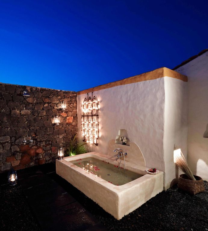 Luxuriöses Badezimmer im Freien mit Wanne und beleuchteten Steinwänden bei Nacht