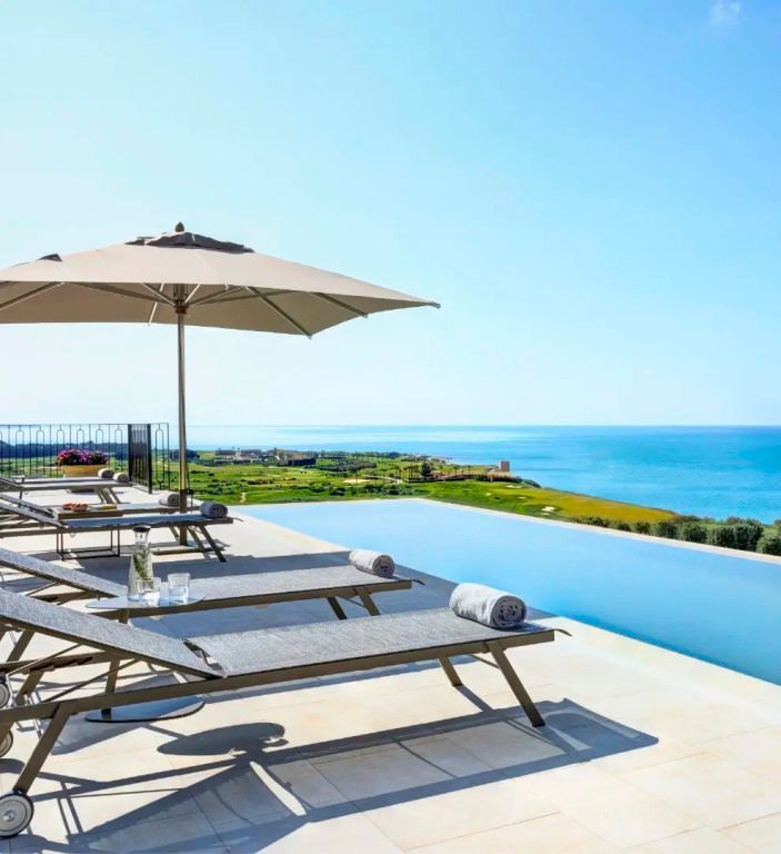 Infinity-Pool mit Liegestühlen und Sonnenschirmen, Blick auf das Meer
