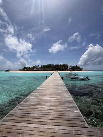 Holzsteg über türkisfarbenem Wasser mit Blick auf die palmenbestandene Insel Vabbinfaru