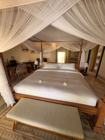 immelbett mit Moskitonetz und Frangipaniblüten in einer Beach Villa aus hellem Holz