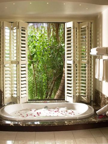 Luxuriöses Badezimmer mit Whirlpool, Fensterläden und Blick auf tropische Vegetation.