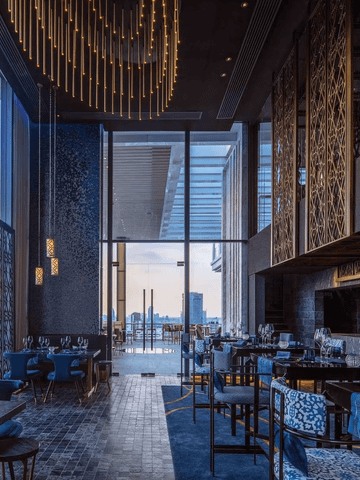 Das Restaurant der 137 Pillars Suite Bangkok besticht durch ein elegantes, modernes Interieur mit warmen Holztönen und stilvollen Details. Große Fenster lassen viel Tageslicht herein