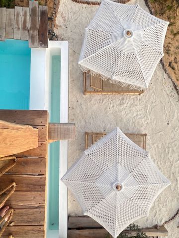 Zwei weiße Sonnenschirme auf Sand neben einem Pool mit Holzsteg.