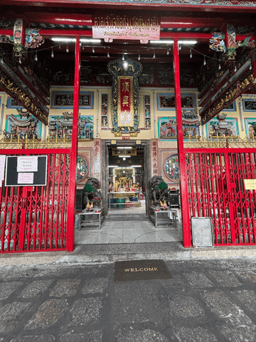 Ein reich verzierter Eingang mit roten Säulen, goldenen Schriftzeichen und kunstvollen Drachenornamenten markiert den Zugang zu einem chinesischen Tempel in Bangkok.
