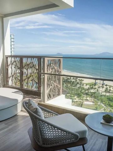 Balkon mit Liegebett, Stuhl und Blick auf den Sandstrand, Palmen und das Meer.