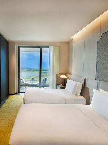 Modernes Doppelzimmer mit zwei Betten, hellem Teppich und Balkon mit Aussicht.