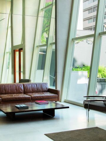 Lounge mit braunem Ledersofa, Sessel und großer Fensterfront mit Blick nach draußen.