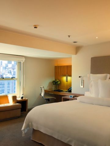 Helles Hotelzimmer mit großem Doppelbett, Schreibtisch und Sitzgelegenheit am Fenster.