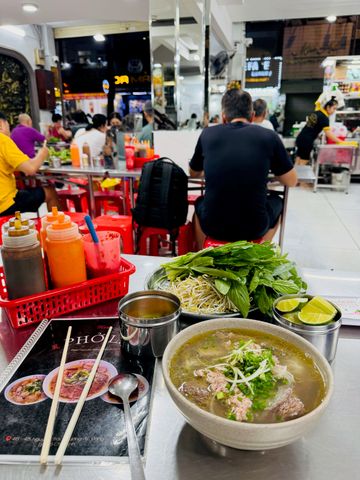 Vietnamesische Suppe Pho mit frischen Kräutern und Limetten in einem belebten Restaurant