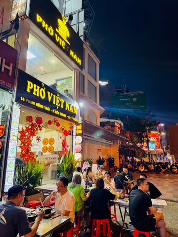 Straßencafé mit Gästen, die bei Nacht vietnamesische Küche genießen