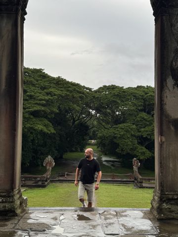 Mann wandert durch einen Tempel mit grünem Garten im Hintergrund.