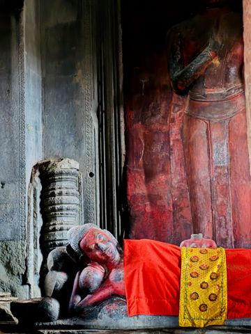 Ruhevolle rote Buddha-Statue neben einer Säule mit kunstvollem Muster im Tempel.