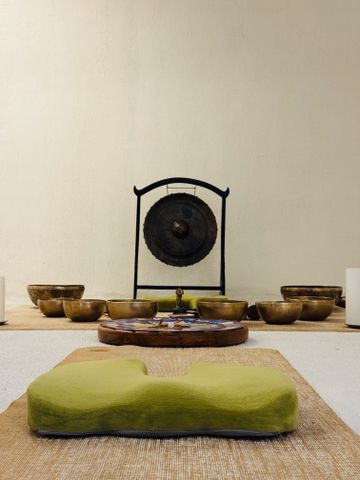Meditationsraum mit Klangschalen, Gong und grünem Kissen auf Holzmatte