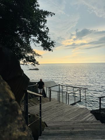 Holzterrasse mit Meerblick bei Sonnenuntergang und Person am Geländer