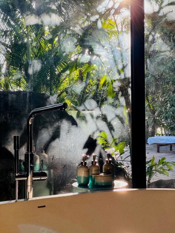 Duftflakons neben Badewanne mit Waldsicht durch Fenster im Morgenlicht.