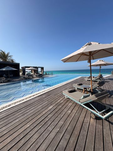 Luxuriöse Sonnenliegen am Pool mit Blick auf das azurblaue Meer bei wolkenlosem Himmel