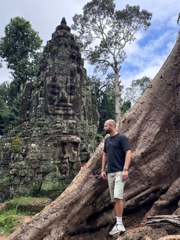 Mann lehnt entspannt an einem uralten Baum mit geschnitztem Tempelturm im Hintergrund.