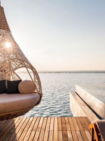 Geflochtener Hängesessel mit Kissen neben einem Pool. Blick auf das Meer.