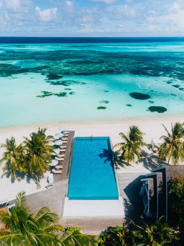 Infinity-Pool an einem Sandstrand mit türkisfarbenem Meer und blauem Himmel