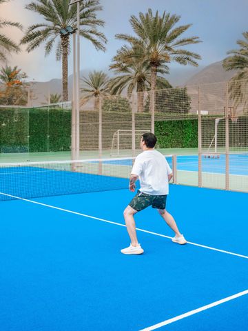 Zwei Personen spielen Tennis auf einem blauen Tennisplatz mit Palmen