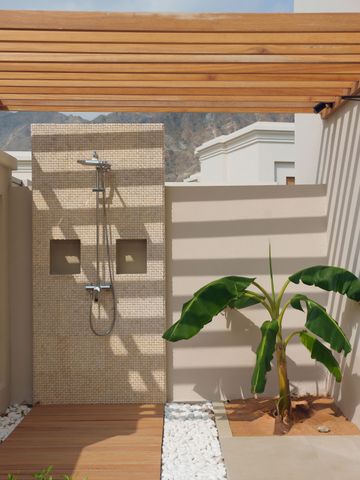 Moderne Außendusche mit Holzelementen und einer Pflanze im Hintergrund