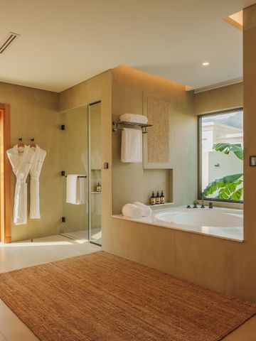 Luxuriöses Badezimmer mit Badewanne, Glasduschkabine und Blick auf tropische Pflanzen.