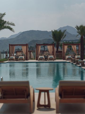 Luxuspool mit Sonnenliegen und Pavillons vor Bergkulisse