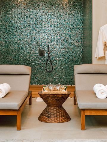 Zwei Liegen mit Handtüchern vor einer Wand mit Mosaikfliesen in einem Spa-Raum