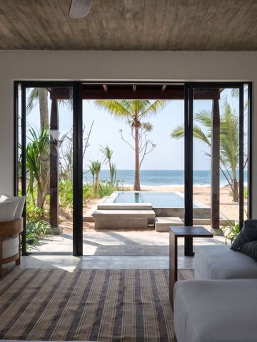 Offener Wohnbereich mit Blick auf Pool und Strand mit Palmen.