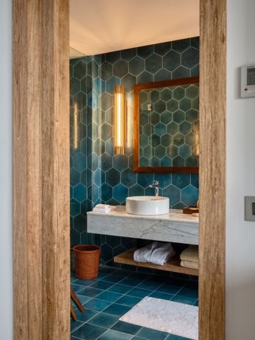 Badezimmeransicht mit blauen Fliesen und beleuchtetem Spiegel.