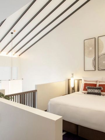 Hell gestaltetes Zimmer mit Doppelbett unter hohen Decken