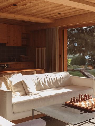 Wohnzimmer mit Sofa und Schachbrett vor einem großen Fenster mit Gartenaussicht