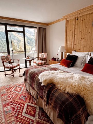 Gemütliches Hotelzimmer mit Holzdekor und flauschiger Wolldecke. Große Fenster mit Bergblick.