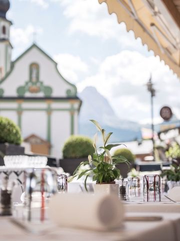 Elegant gedeckter Tisch auf einer Terrasse mit Bergblick und Kirche im Hintergrund
