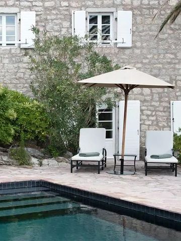 Außenansicht mit Pool, Steinmauer und Liegestühlen unter einem Sonnenschirm.