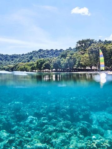 Türkises, klares Wasser mit üppig bewaldeten Hügeln und buntem Segelboot am Horizont