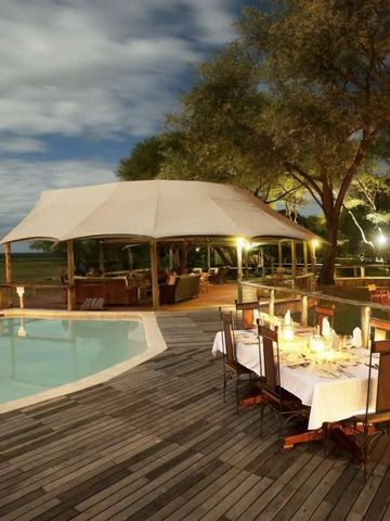 Elegantes Abendessen im Freien neben einem beleuchteten Pool mit Zeltdach im Anabezi Camp