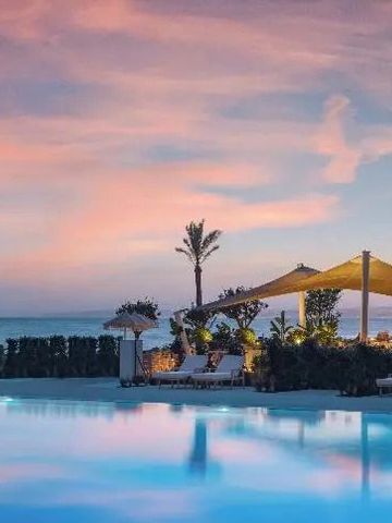 Infinity Pool mit Meerblick bei Sonnenuntergang. Palmen und Lounge-Bereich im Hintergrund.