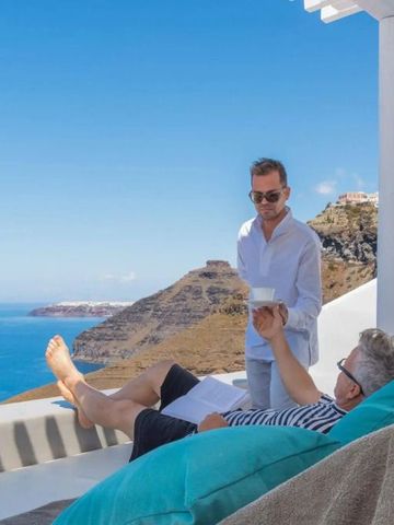 Personen auf Terrasse mit Meerblick. Ein Mann serviert ein Getränk