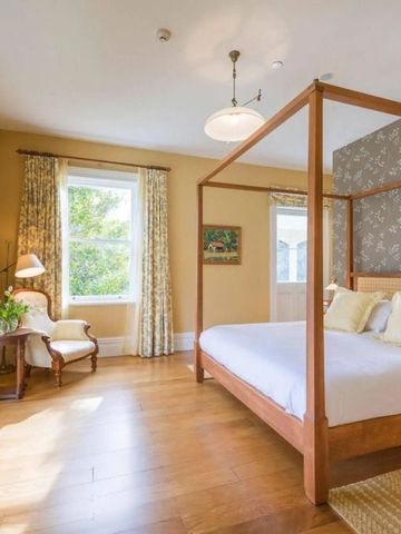 Geräumiges Schlafzimmer mit Himmelbett und großen Fenstern in warmen Farbtönen.
