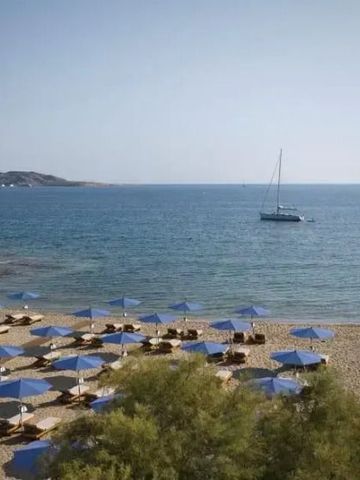 Traumhafter Strand mit blauen Sonnenschirmen, klarem Meer und Segelboot am Horizont