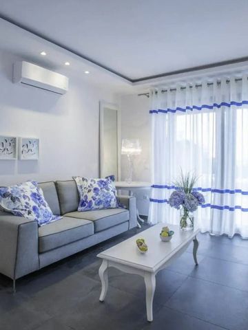Helles Wohnzimmer mit grauem Sofa und blauen Kissen vor einem großen Fenster