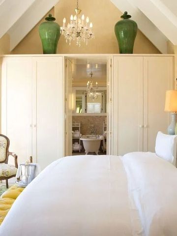 Schlafzimmer mit hoher Decke, Kronleuchter und Badewanne im Hintergrund.