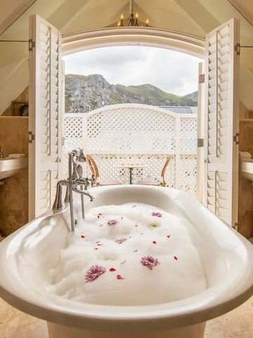 Luxuriöse Badewanne mit Blick auf die Natur durch geöffnete Fensterläden