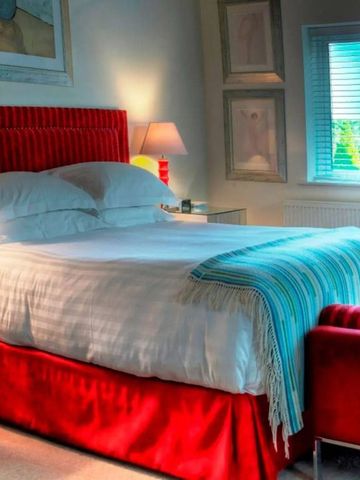 Helles und elegantes Hotelzimmer mit rotem Bett und moderner Kunst.