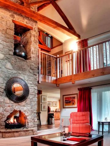 Gemütliches Wohnzimmer mit steinernem Kamin und Holzbalkendecke.