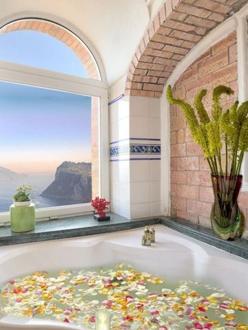 Luxuriöses Badezimmer mit Blick auf das Meer, gefüllt mit Blütenblättern.