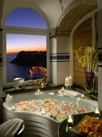 Romantisch beleuchtetes Badezimmer bei Sonnenuntergang mit Blütenblättern im Wasser.