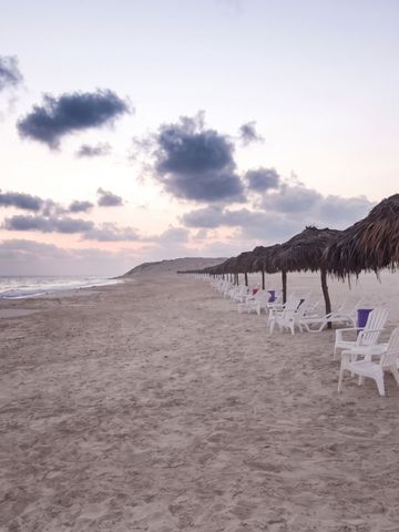 Leerer Sandstrand mit Liegestühlen und Strohdächern bei bewölktem Himmel